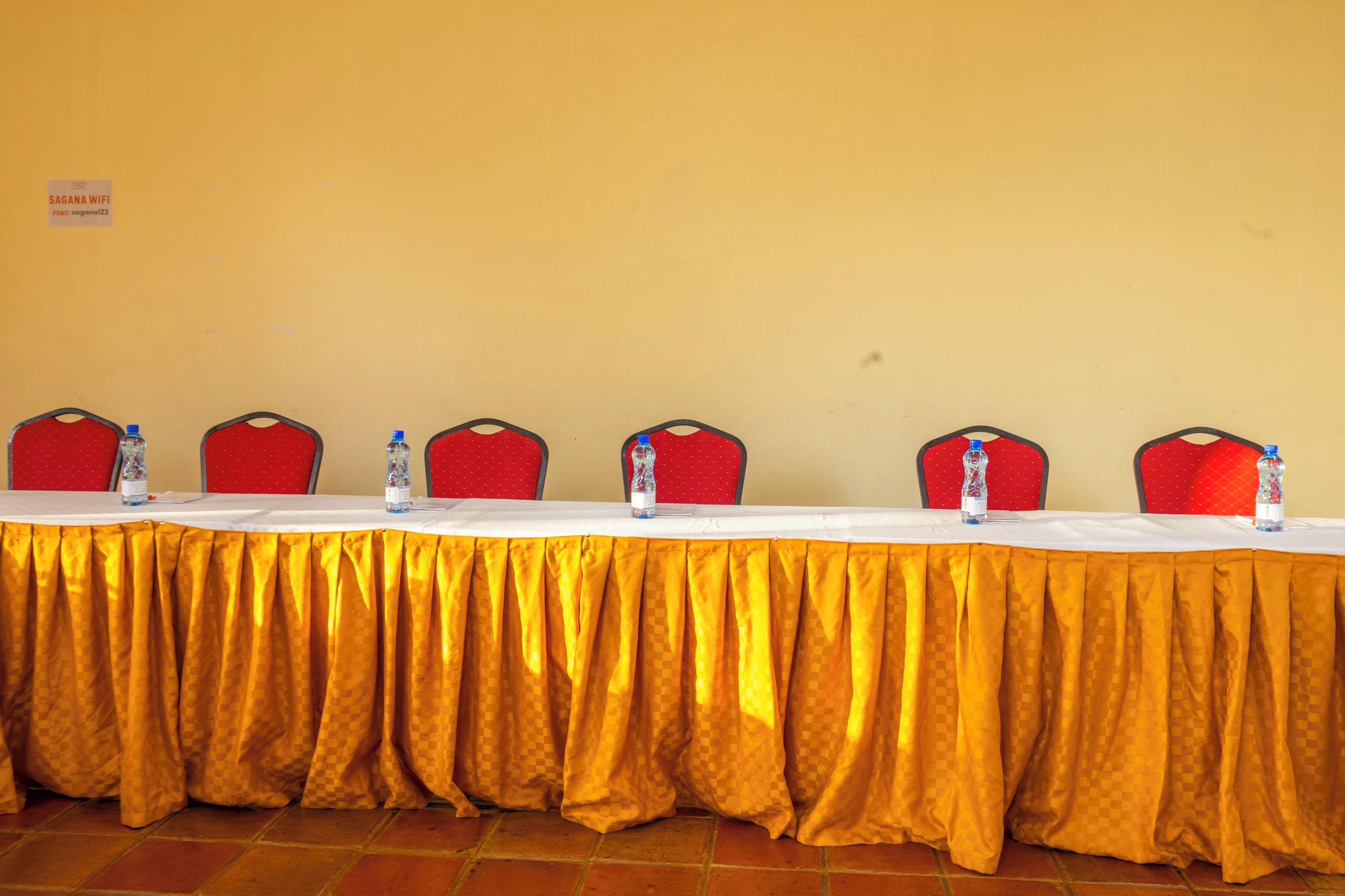 Una mesa de conferencias con mantel amarillo, sillas rojas y botellas de agua.