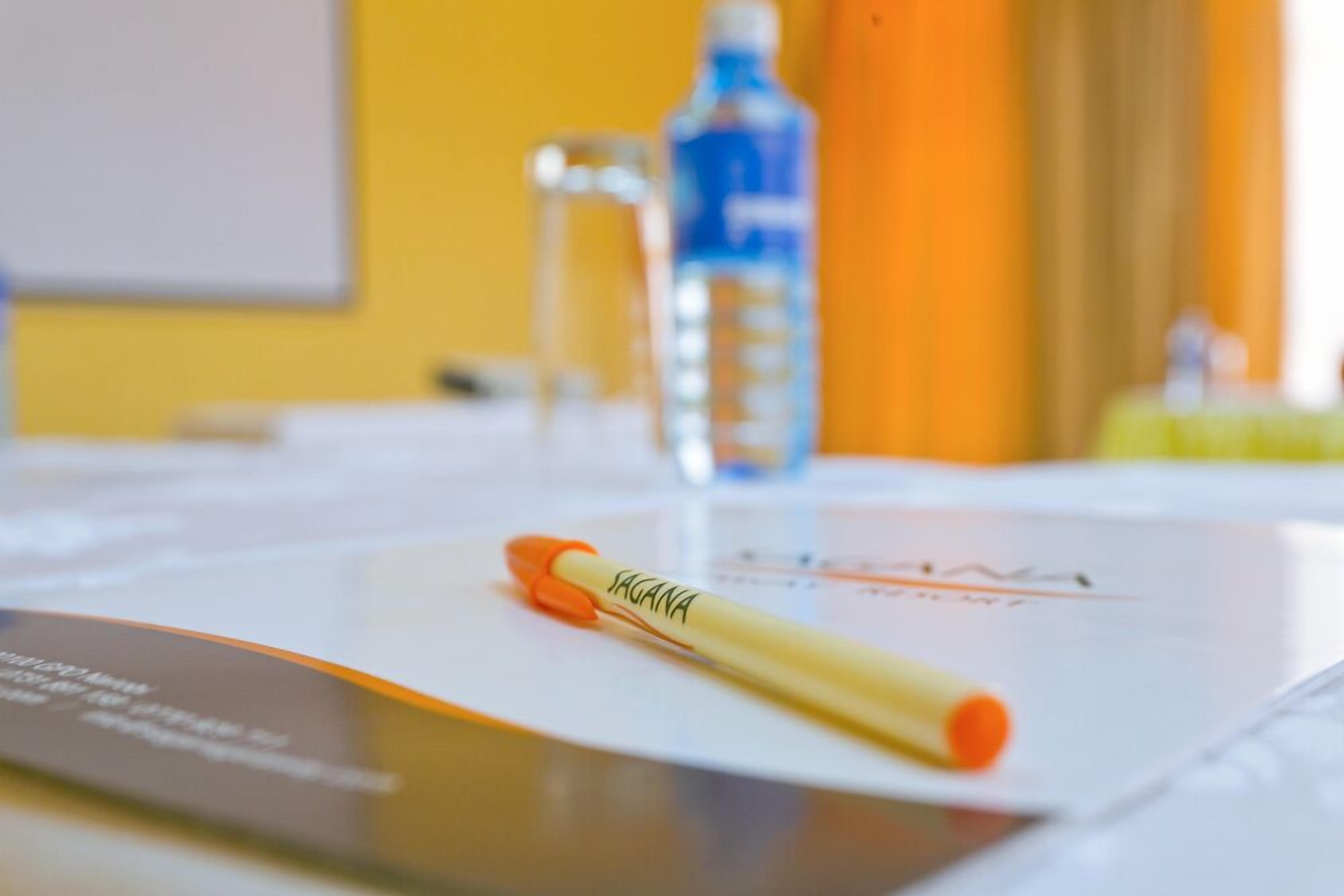 A blurred hotel room with a bed, a water bottle, and a pen on a piece of paper.