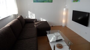 A living room with a sofa, a glass coffee table, a TV, and artwork on the wall. - Stars Berlin Apartments Waldstrasse (Berlin)