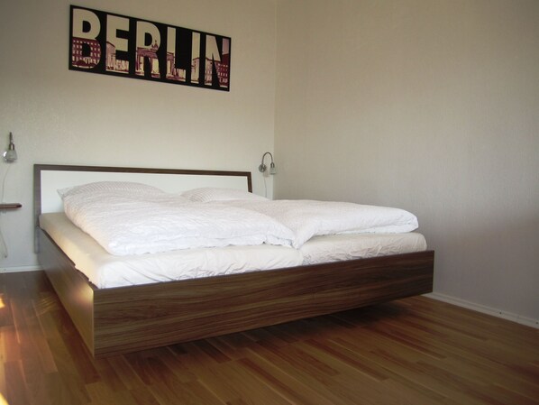 A modern bedroom with a wooden bed frame, white bedding, and a wall-mounted sign that reads "BERLIN". - Stars Berlin Apartments Waldstrasse (Berlin)