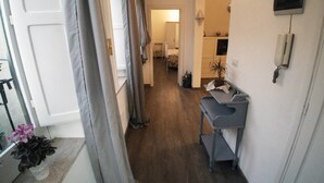 A narrow hallway with a desk and a telephone on the right, leading to a bedroom with a bed and a nightstand.