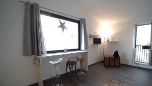 A room with a desk, two chairs, a star decoration on the window, a radiator, a suitcase, and a patterned rug.