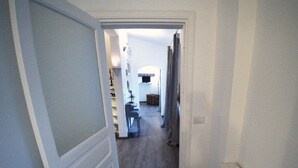A hallway with a door on the left, a desk with a chair, and a bed in the distance.