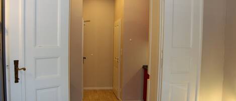 A hallway with white doors, a wooden floor, and a small trash bin.