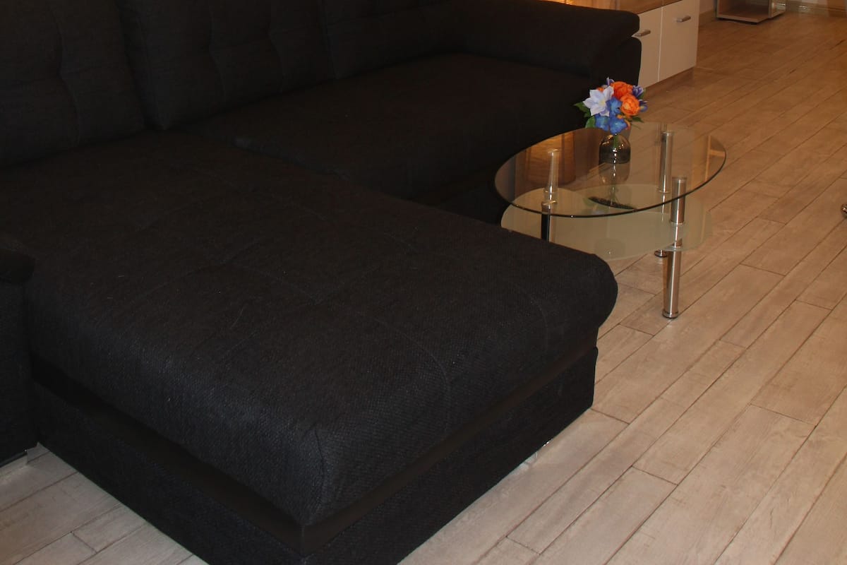 Ein modernes Wohnzimmer mit einem schwarzen Ecksofa, einem Glastisch und einem Holzschrank.