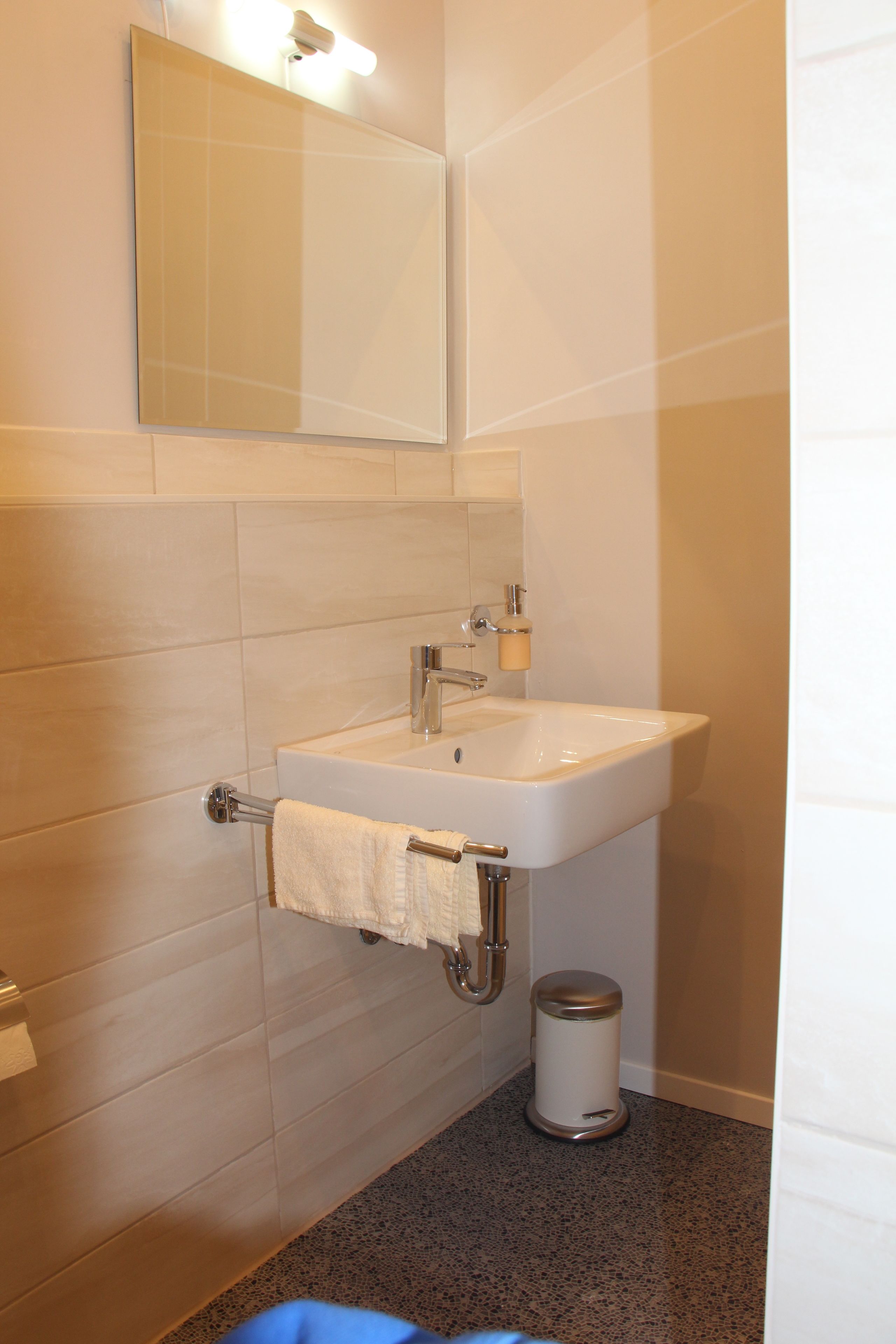 A bathroom with a white sink, a mirror, and a trash can.