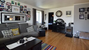 A living room with a grey sofa, a coffee table with decorative items, a kitchen area with a stove, and a dining table. - Solferie Holiday Home- Gullveien (Kristiansand)