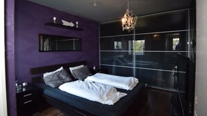 A modern bedroom with a large bed, a nightstand, a mirror, and a chandelier. - Solferie Holiday Home- Gullveien (Kristiansand)