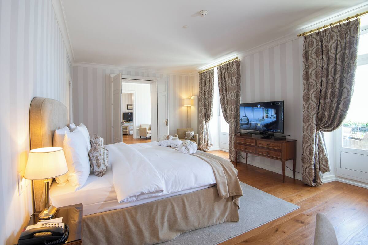 Ein Hotelzimmer mit einem Bett, einem Fernseher, einem Schreibtisch mit Lampe und Vorhängen.