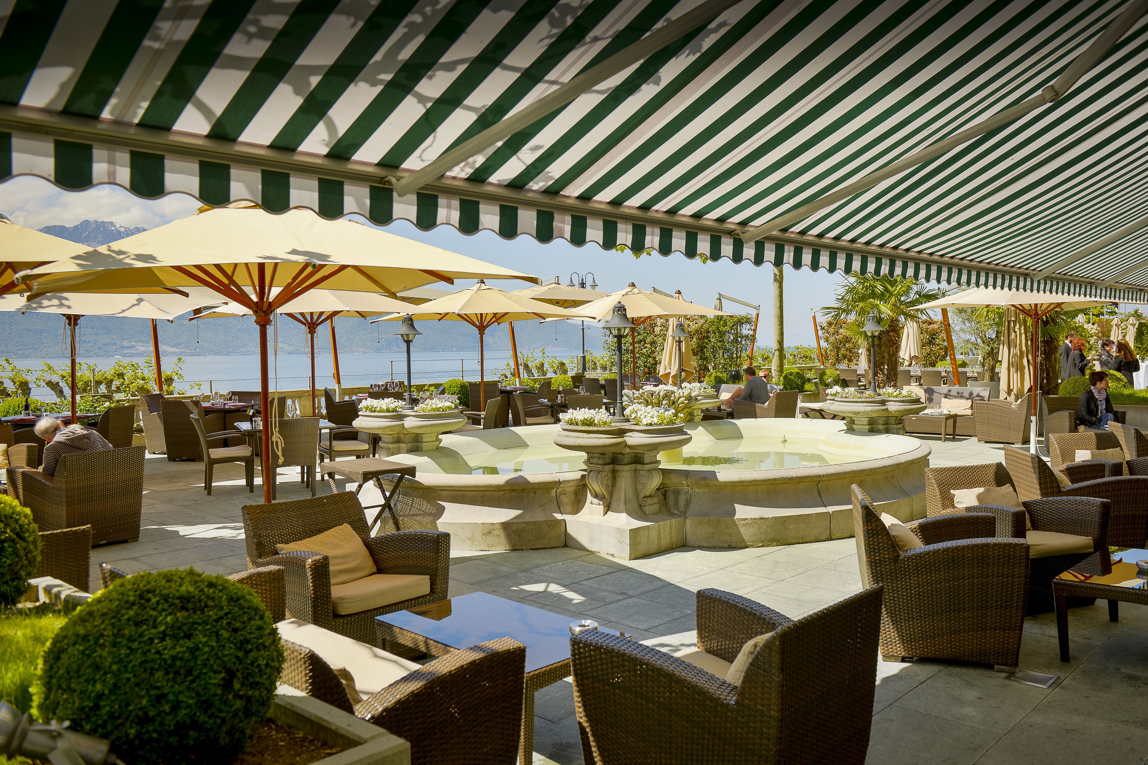 An outdoor patio with wicker furniture, umbrellas, and a fountain.