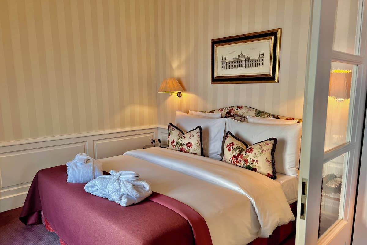 Ein Hotelzimmer mit einem ordentlich bezogenen Bett, einem gerahmten Bild an der Wand und einem Fenster mit Vorhängen.