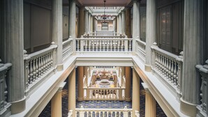 Un intérieur somptueux, à plusieurs niveaux, avec des colonnes de marbre, un grand piano et un sol à carreaux.
