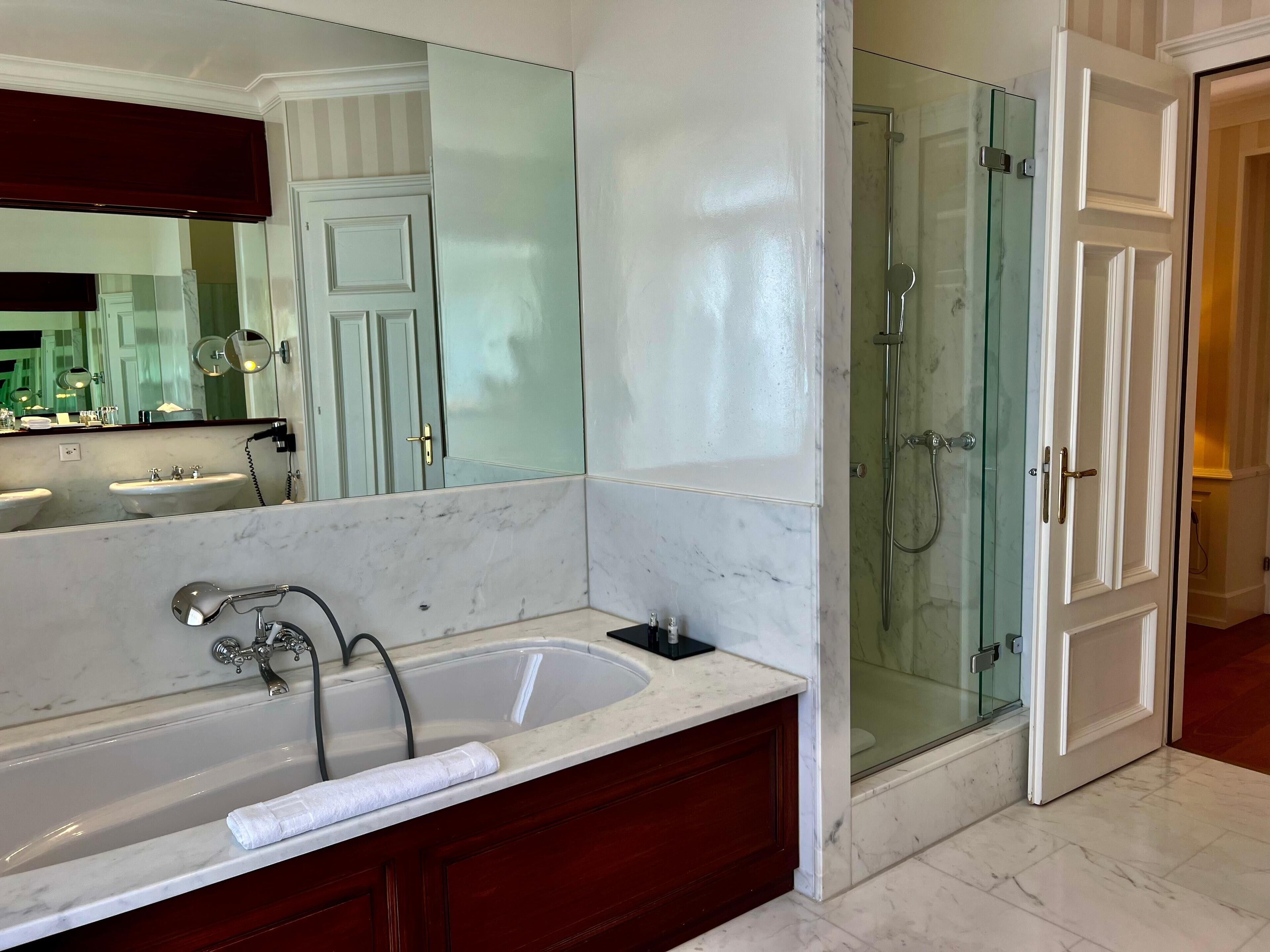 Une salle de bain moderne avec un lavabo en marbre, une baignoire, une douche à l’italienne et un grand miroir.