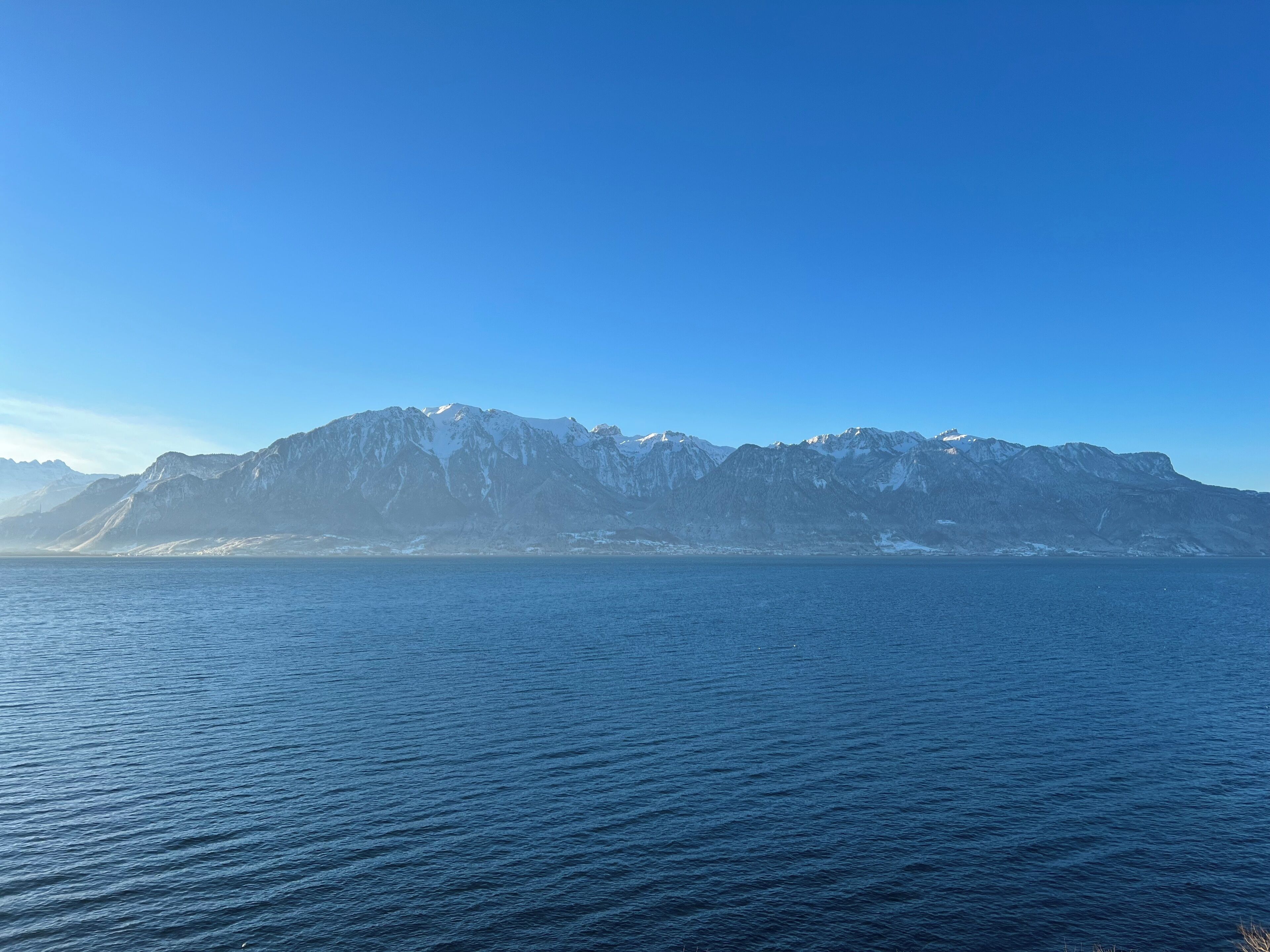 Une chaîne de montagnes aux sommets enneigés, avec une mer calme en premier plan.