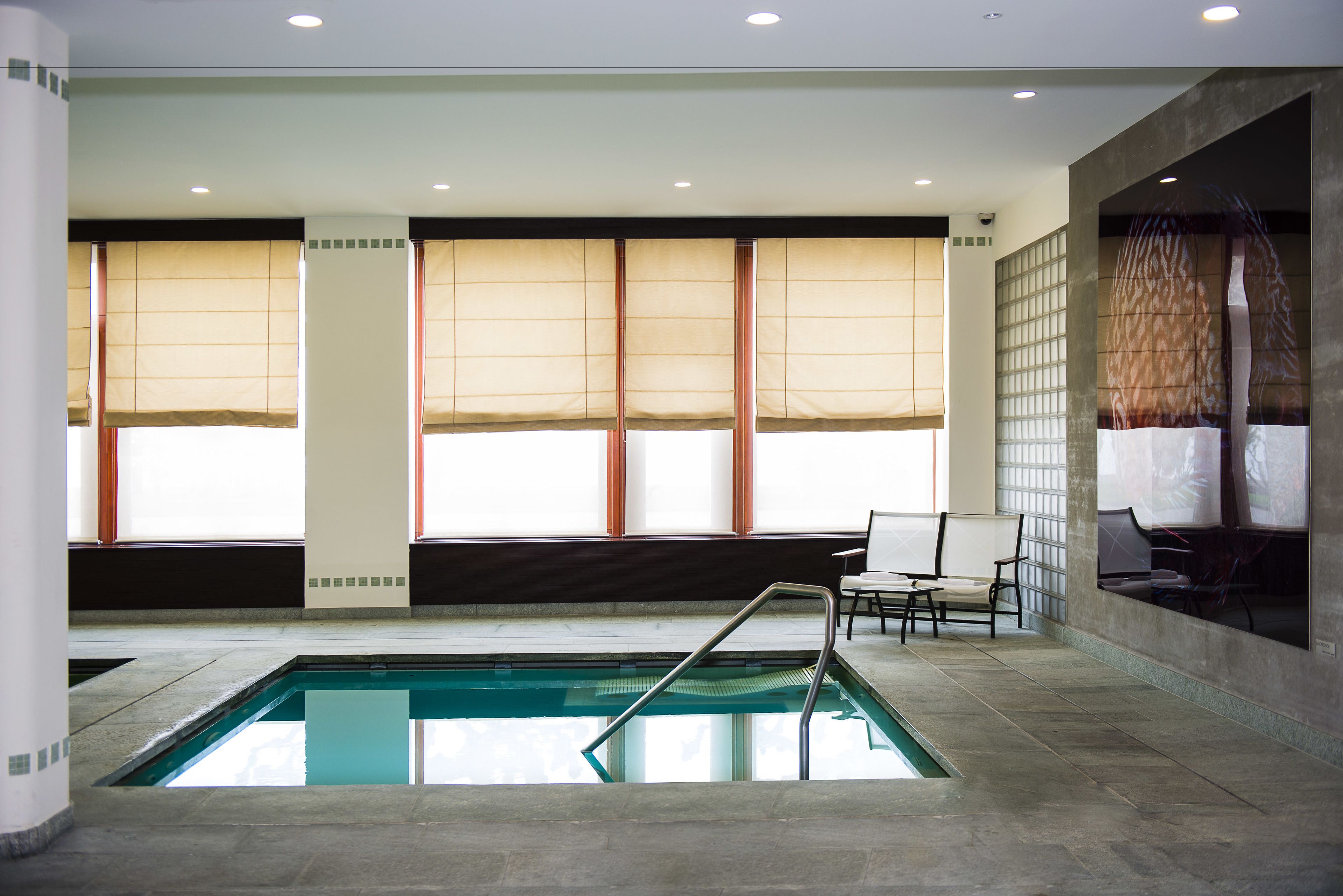 Une piscine intérieure offrant une vue sur la ville grâce à de grandes fenêtres, un espace détente avec des fauteuils et un design architectural moderne.