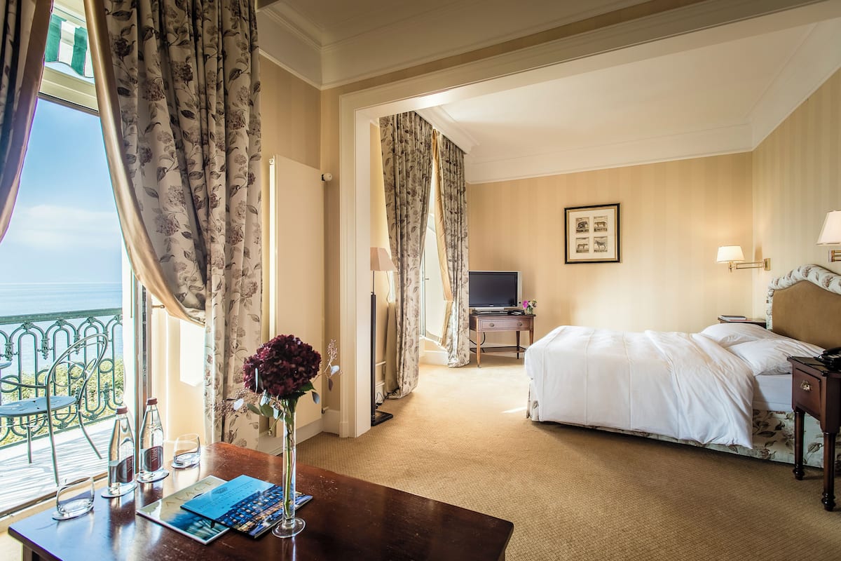 Ein Hotelzimmer mit Bett, Schreibtisch mit Blumenvase, Fernseher und Balkon mit Blick.