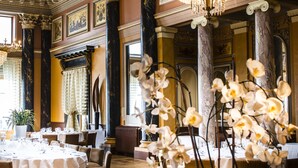 Una sontuosa sala da pranzo con lampadari elaborati, colonne di marmo e una raffinata tavola imbandita.