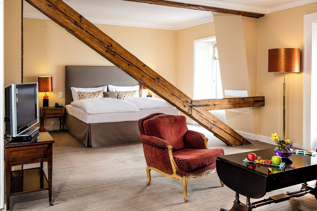 Ein Hotelzimmer mit einem Bett, einem roten Sessel, einem Schreibtisch mit Lampe und einem Fernseher.