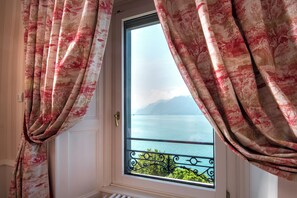 Una ventana con cortinas, vista a un cuerpo de agua y barandilla de balcón.