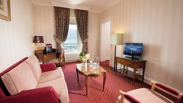 Hotelkamer met een rood tapijt, een bank, een stoel, een kleine tafel met een vaas, een televisie en een raam met gordijnen.