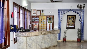 A reception area with a marble counter, framed pictures, and potted plants. - Hotel Vinayakam (Udaipur)