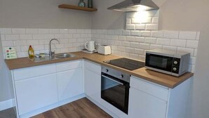 Une cuisine compacte avec des meubles blancs, un plan de travail en bois, un four encastré, un four à micro-ondes et une hotte de cuisine en acier inoxydable.