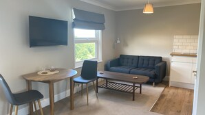 Un espace de vie compact comprenant un canapé, une table à manger et un téléviseur fixé au mur.