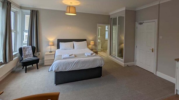 Une chambre à coucher avec un lit, des tables de chevet, une chaise, un miroir et une porte.