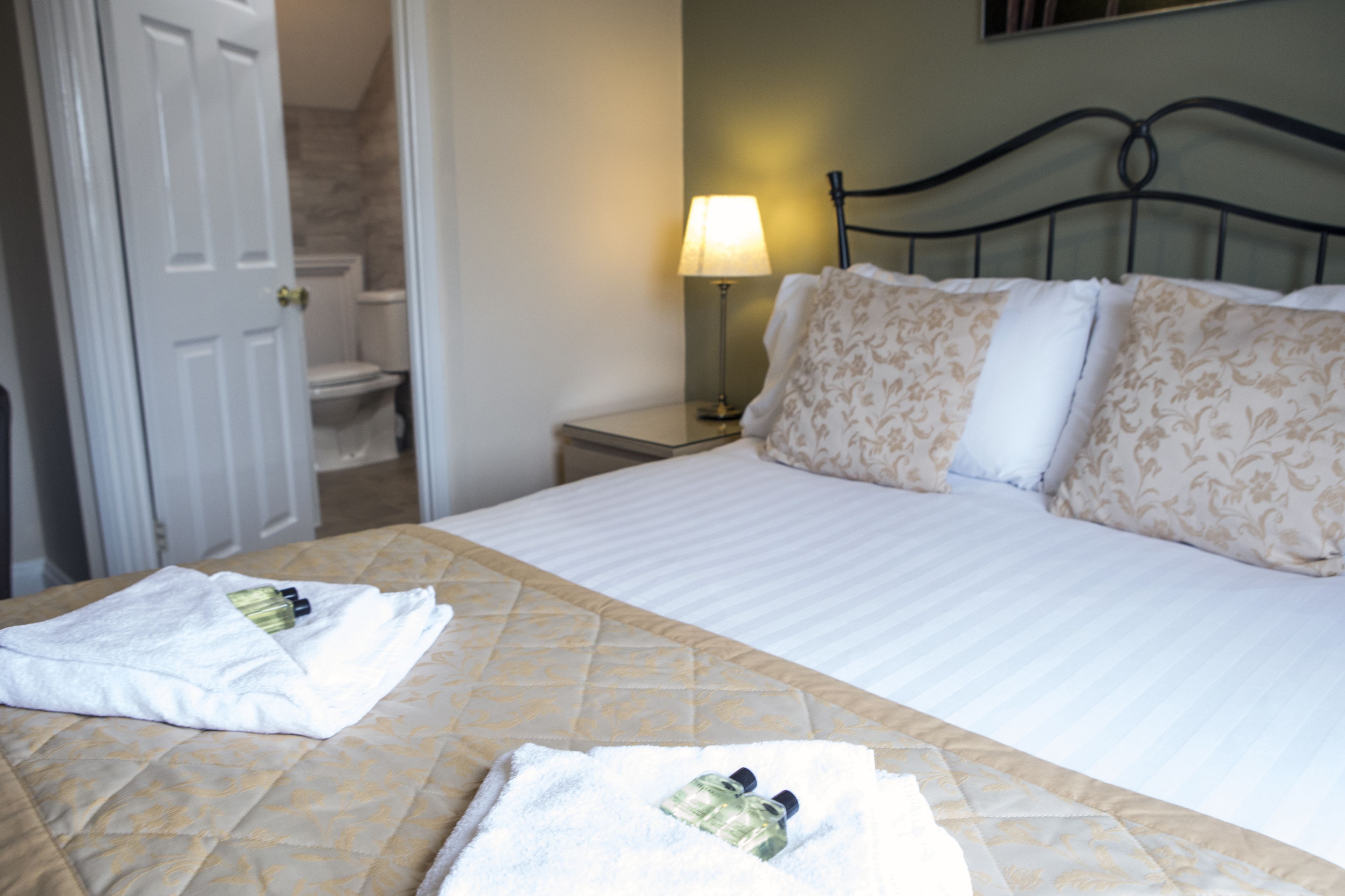 A hotel room with a bed, a nightstand, a lamp, and a bathroom visible through an open door.