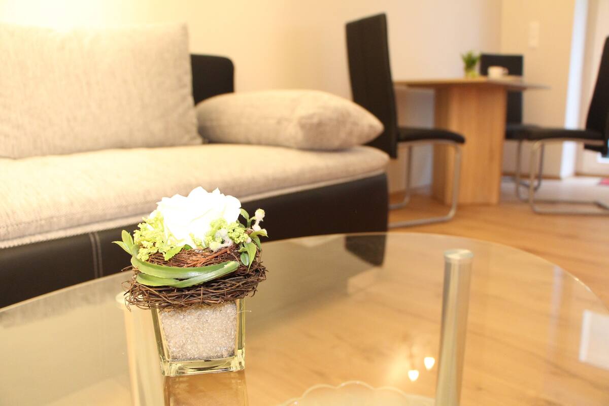A glass table with a decorative centerpiece featuring a nest, green leaves, and white flowers.