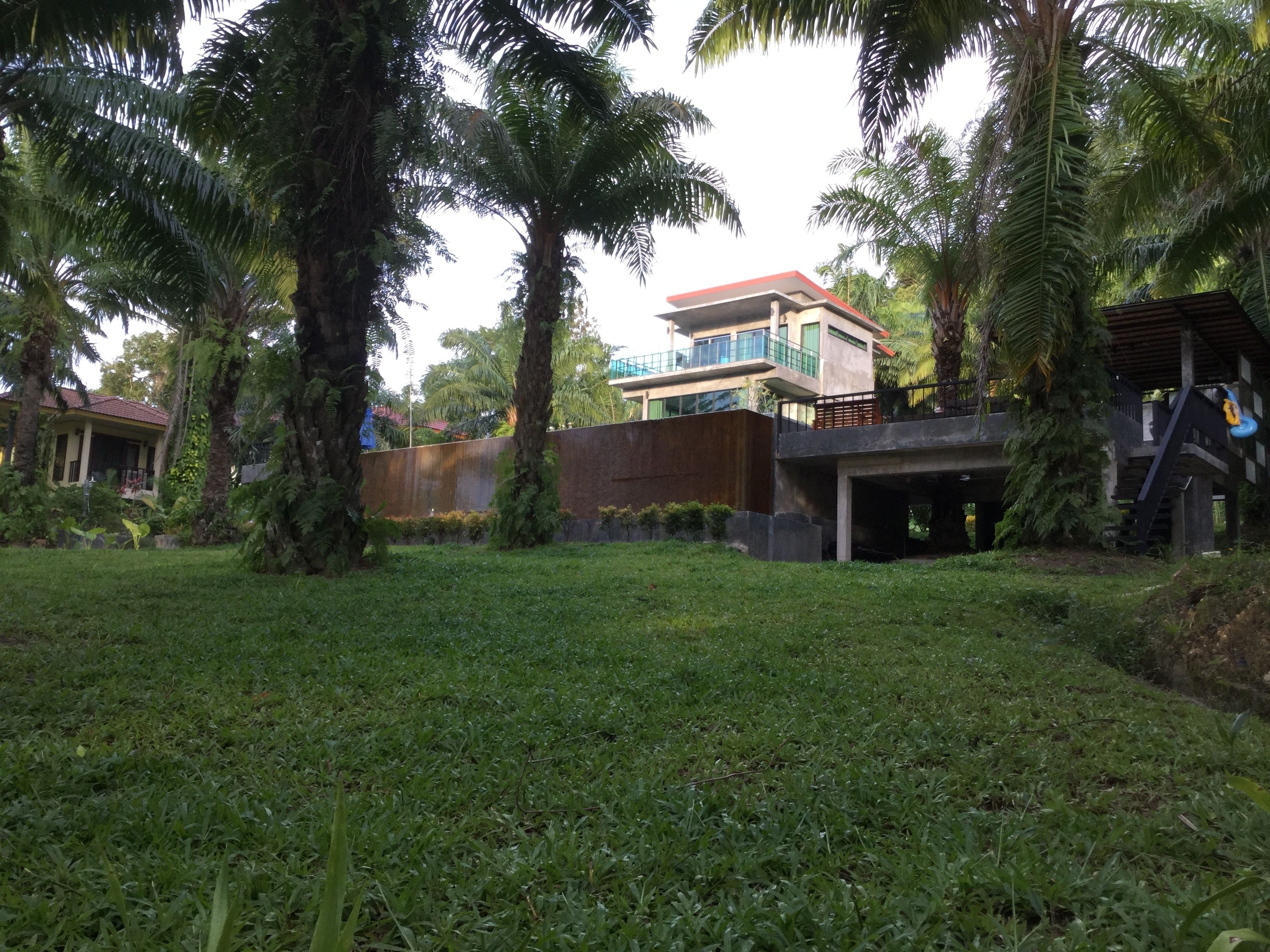 A residential area with a modern two-story house, a covered parking area, and lush greenery.