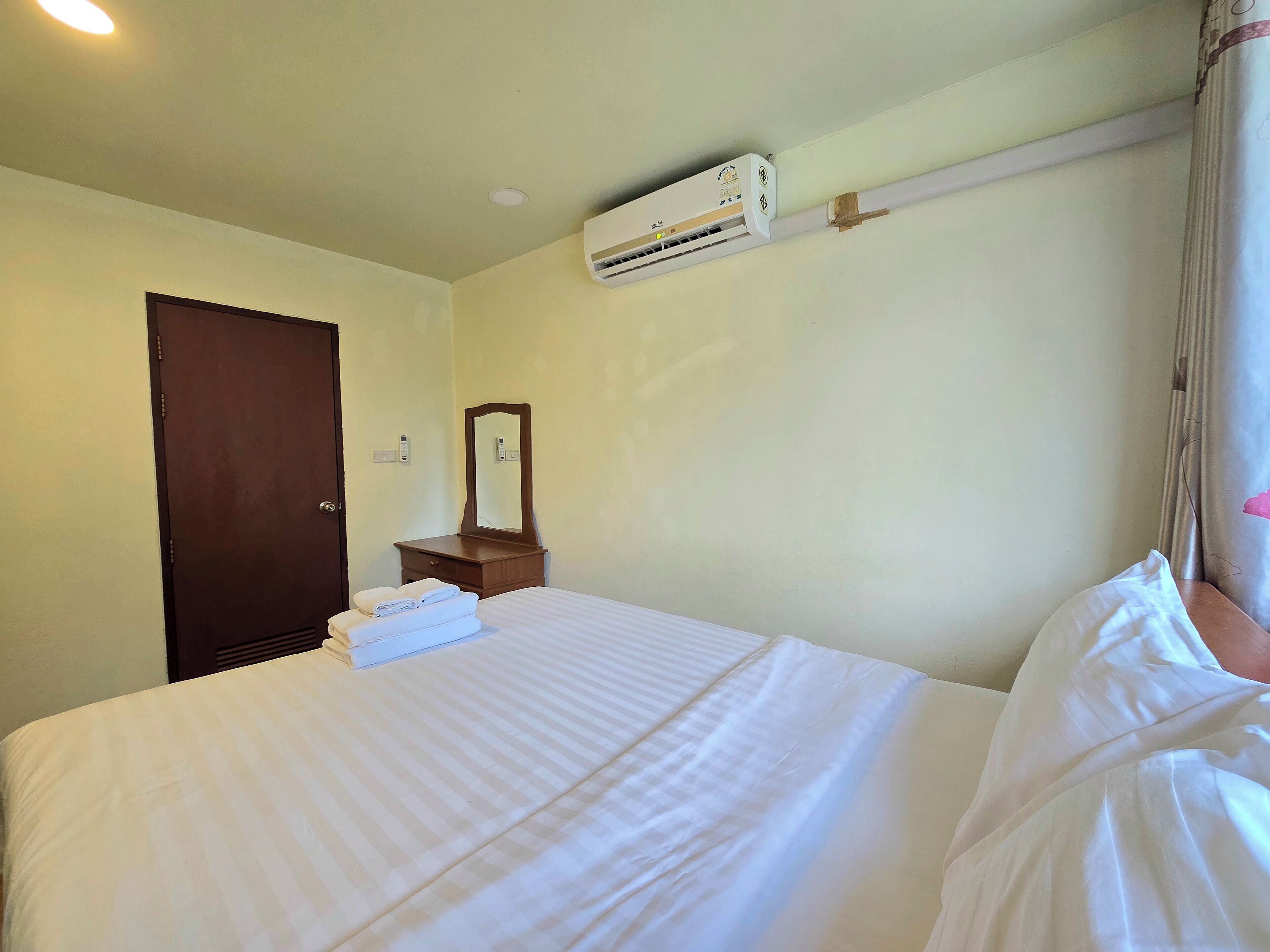 A hotel room with a bed, a dresser, a mirror, an air conditioning unit, and a door.