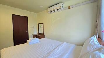 A hotel room with a bed, a dresser, a mirror, an air conditioning unit, and a door.