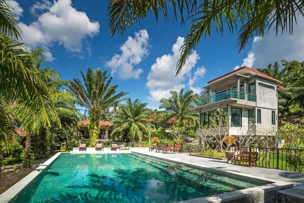 A swimming pool surrounded by lush greenery and a two-story building with a balcony. - Krabi Green Hill Pool Villas (Krabi)