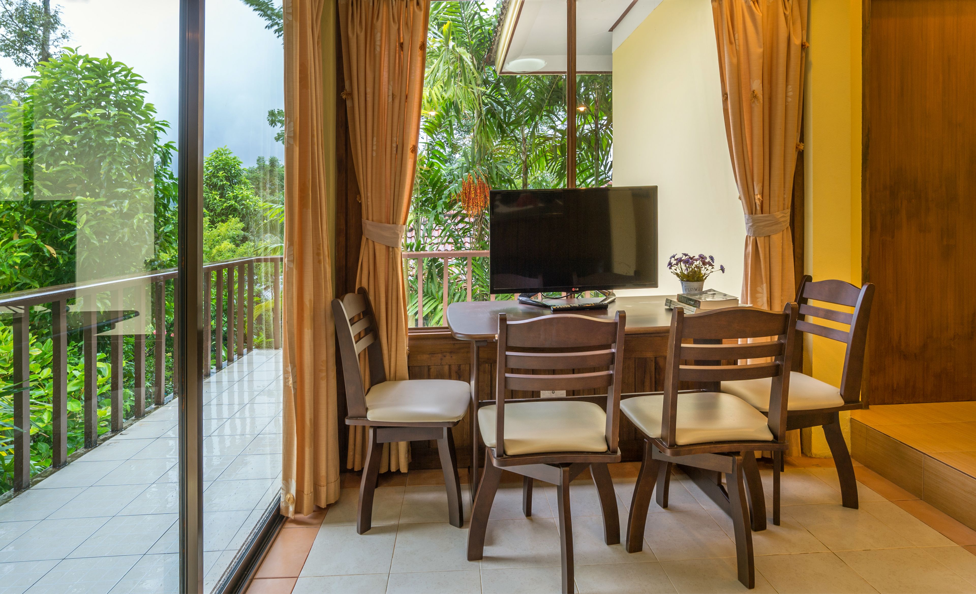 Un balcon équipé d’une table à manger, de chaises, d’un téléviseur à écran plat et d’une plante en pot.