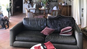 Un salón amplio con techo alto, un sofá de cuero oscuro y un comedor al fondo.