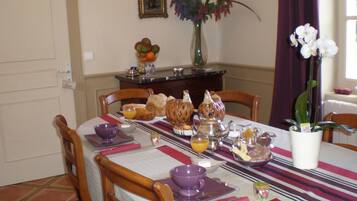 Una mesa de comedor dispuesta con cosas para el desayuno, incluyendo pan, pasteles y un florero con flores.