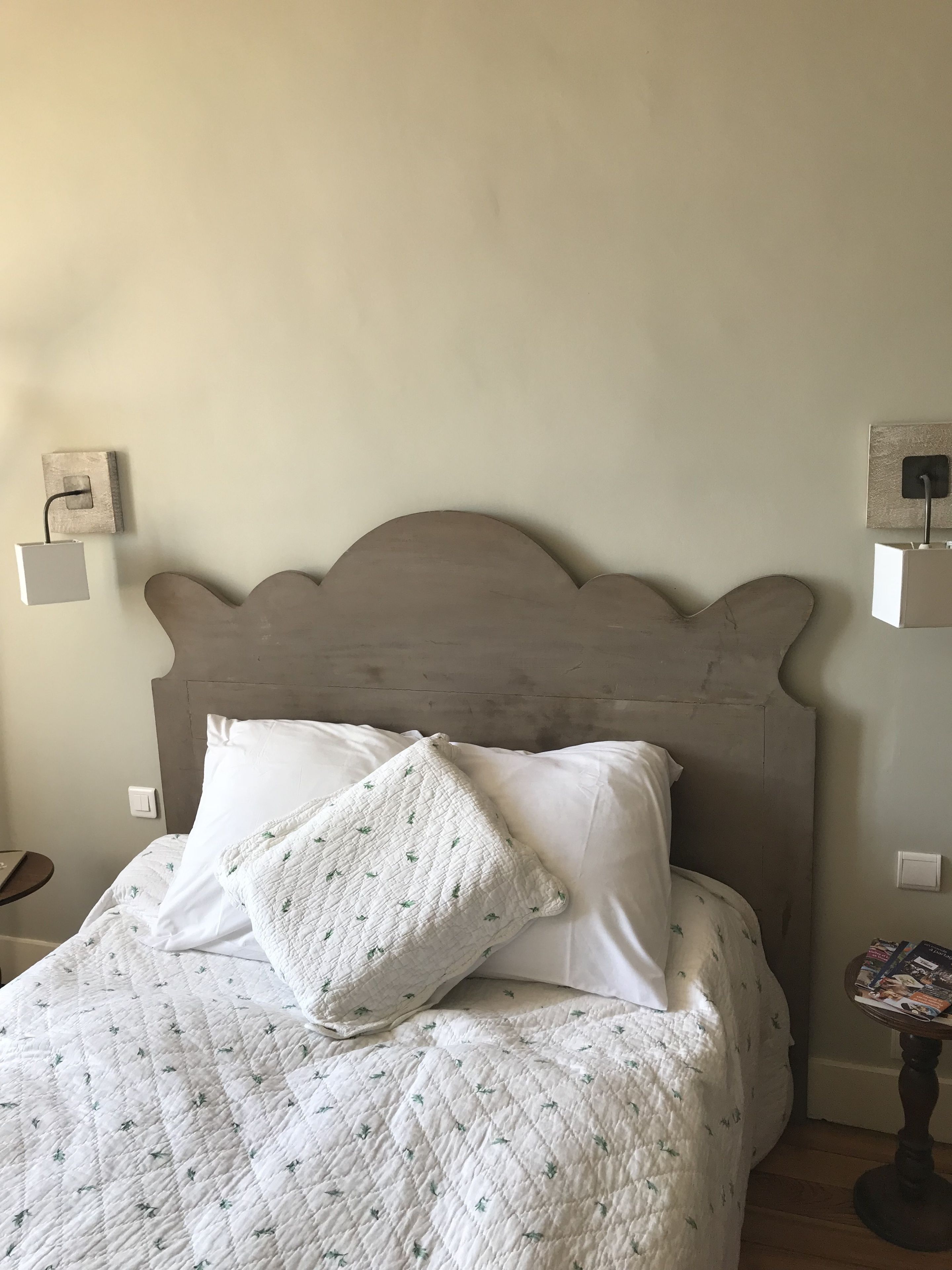 Una cama con edredón blanco acolchado y almohadas, un cabecero de madera y mesitas de noche con lámparas.