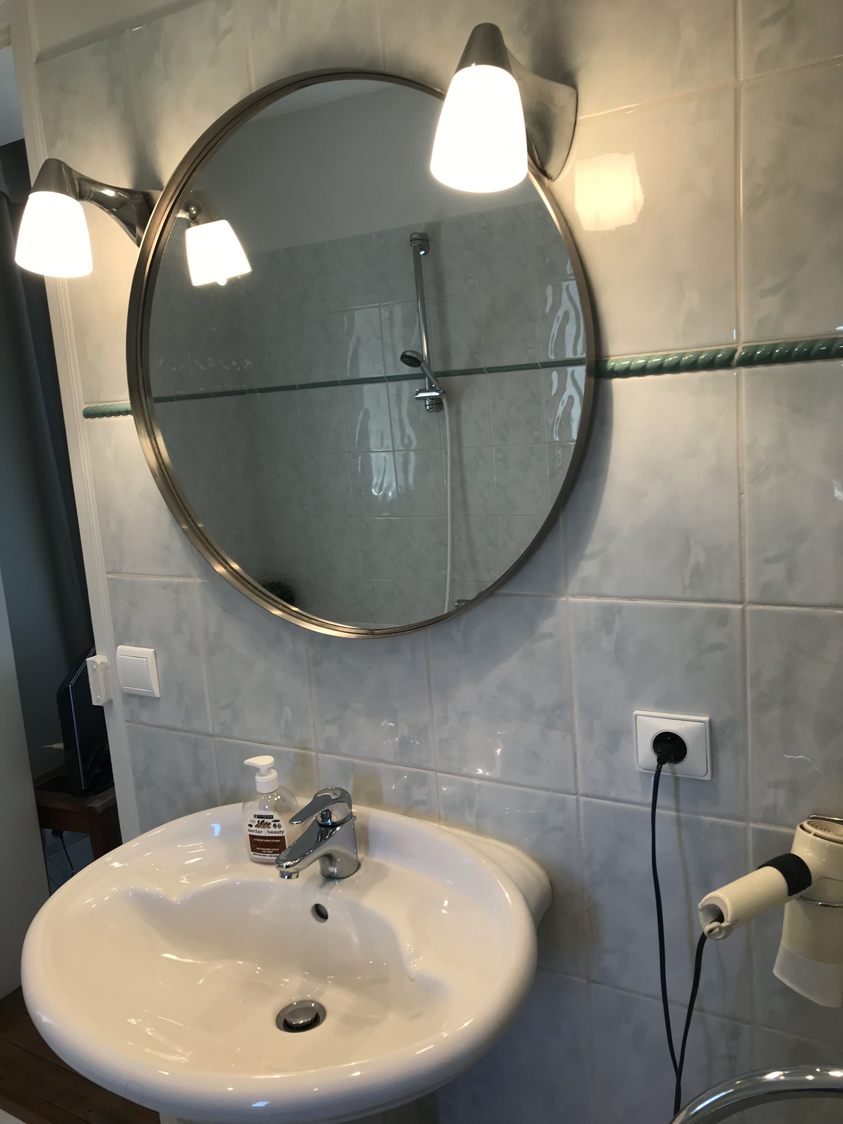 A bathroom with a round mirror, a white sink, and a handheld showerhead.