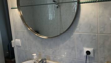 A bathroom with a round mirror, a white sink, and a handheld showerhead.