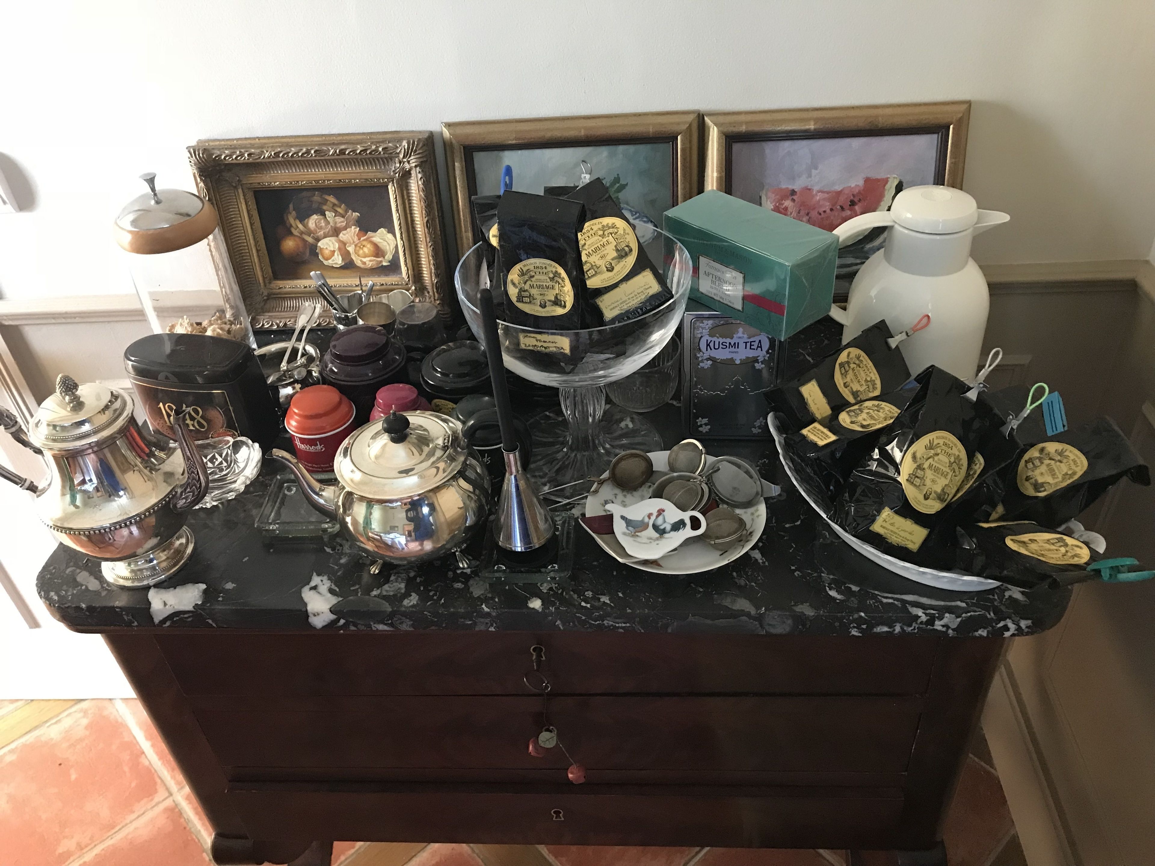 Een rommelig aanrecht met verschillende theeserviezen, een theepot en ingelijste foto's.