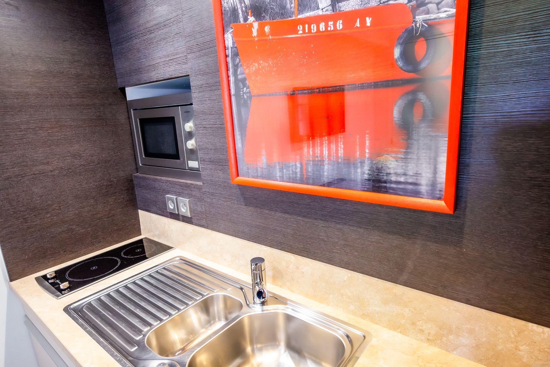 A kitchen with a stainless steel sink, a built-in oven, and a wall-mounted picture.