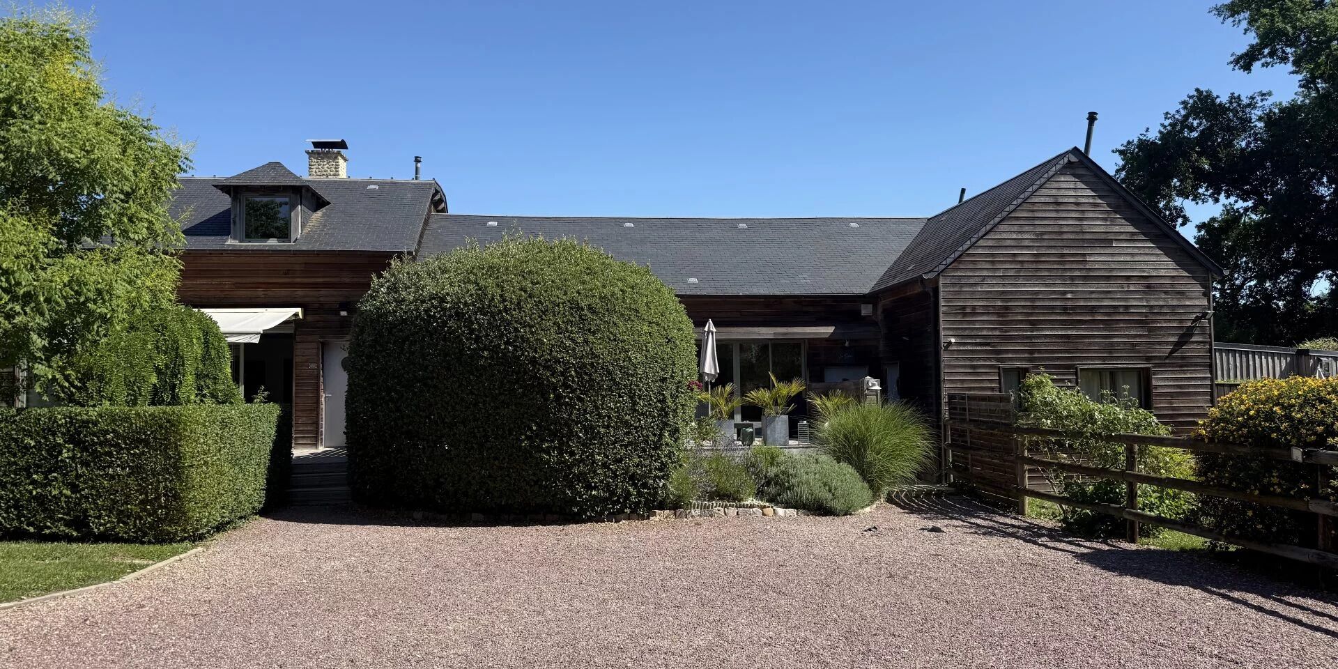 Une maison à deux étages avec une allée en gravier, un revêtement extérieur en bois et un jardin bien entretenu.