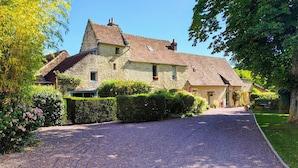 A stone house with a gravel driveway, surrounded by lush greenery and flowering bushes. - Chambres d'Hôtes La Ferme de L'Oudon & Spa (Saint-Pierre-en-Auge)