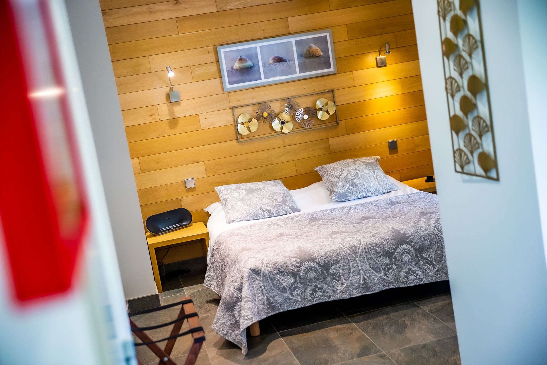 Un dormitorio con cabecera de madera, cama con ropa de cama estampada, mesita de noche y lámpara de pared.