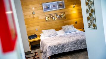 Un dormitorio con cabecera de madera, cama con ropa de cama estampada, mesita de noche y lámpara de pared.