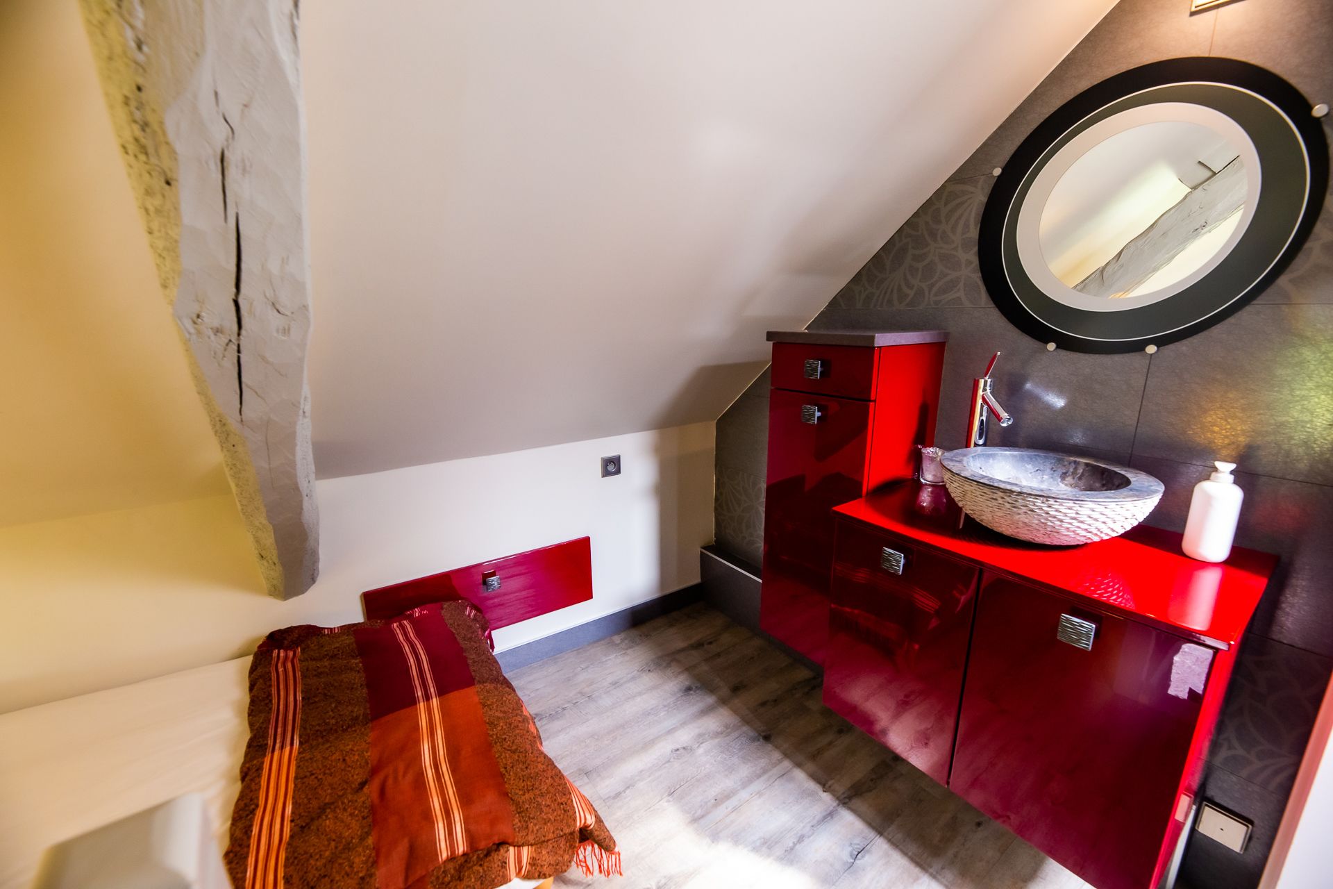 Une chambre avec une coiffeuse rouge, un miroir rond et un plancher en bois.
