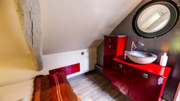 Une chambre avec une coiffeuse rouge, un miroir rond et un plancher en bois.