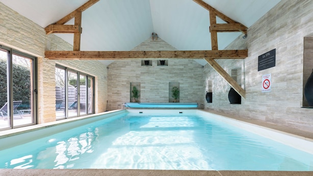 An indoor swimming pool with stone walls and wooden beams, large windows, and a sign indicating a spa area. - Chambres d'Hôtes La Ferme de L'Oudon & Spa (Saint-Pierre-en-Auge)