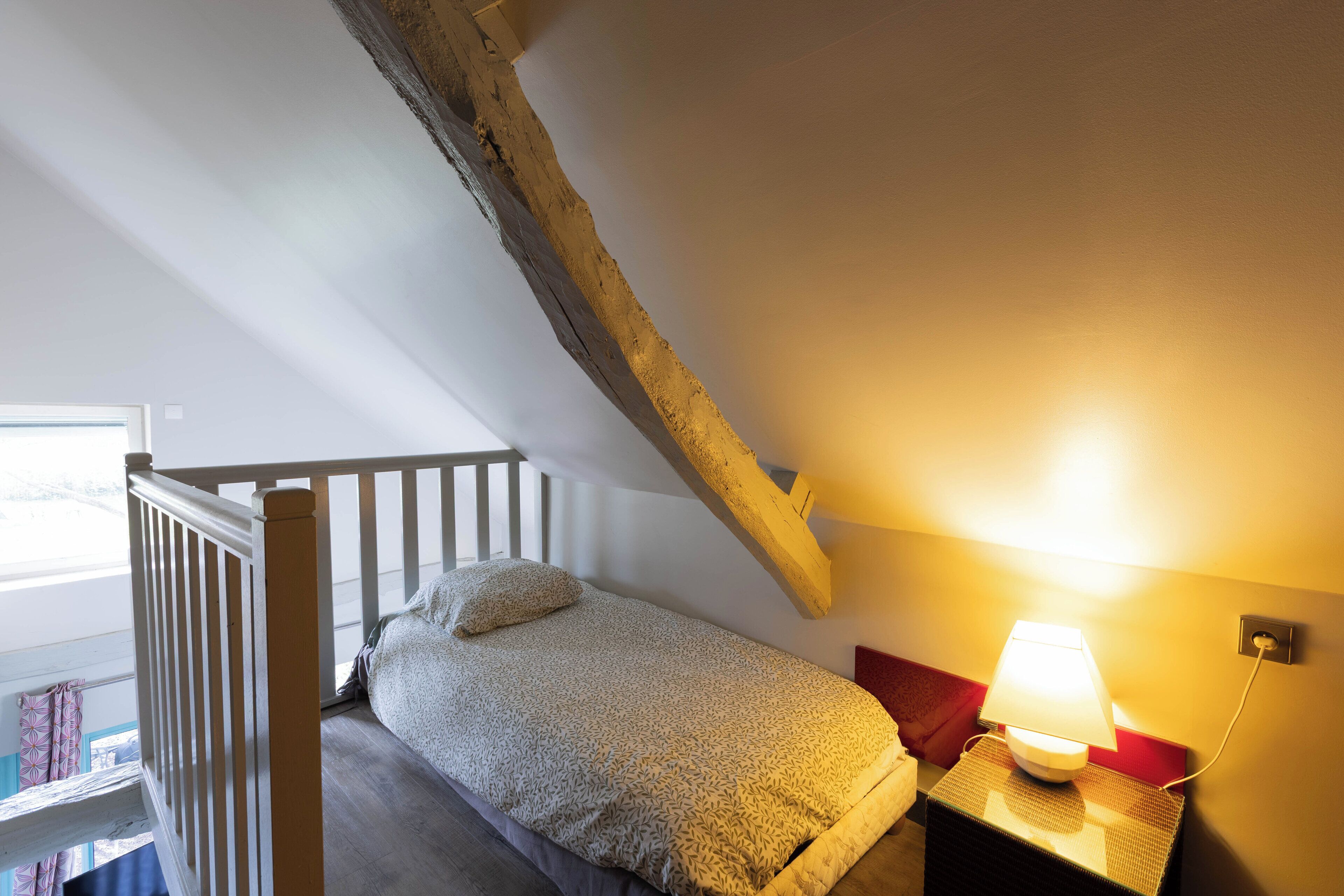 Un dormitorio pequeño con una cama individual, una mesita de noche con lámpara y una viga de madera en el techo.